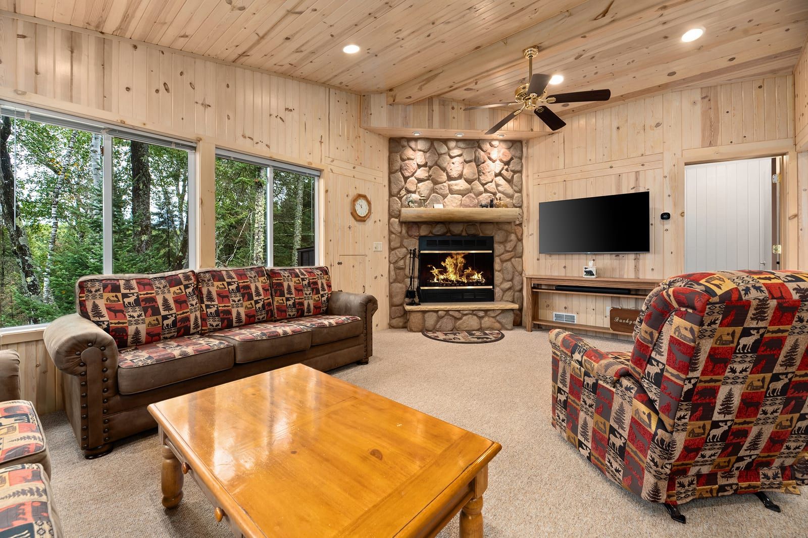 Living room with stone fireplace, TV, and Northwoods decor